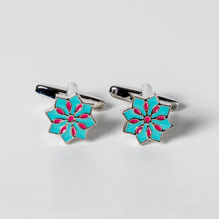A pair of silver-toned cufflinks with an eight-pointed star design. The star is filled with a vibrant teal color, and within it, a smaller eight-pointed design is present in a bright pink hue. The cufflinks are positioned on a white background, slightly angled, showcasing their faces and the clasps. Ethnic Mosaic Cufflinks - Blue